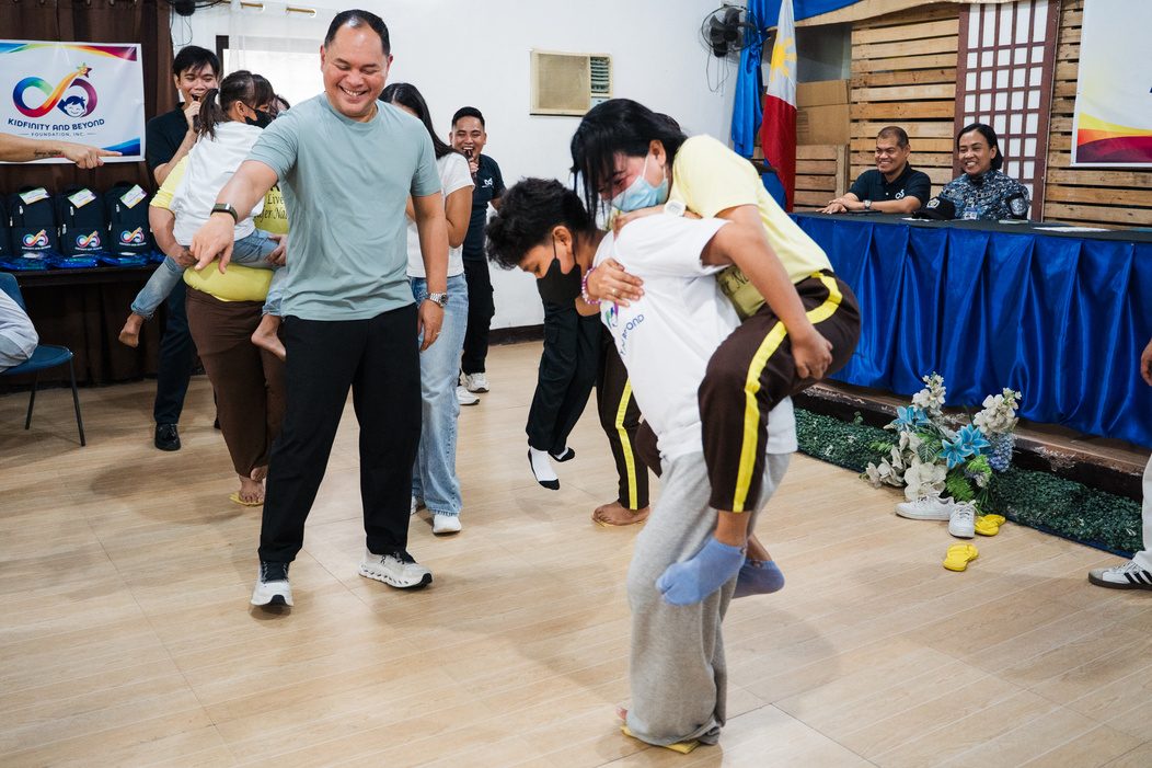 A Foundation staff member plays a game with a child beneficiary on his back, while others watch.