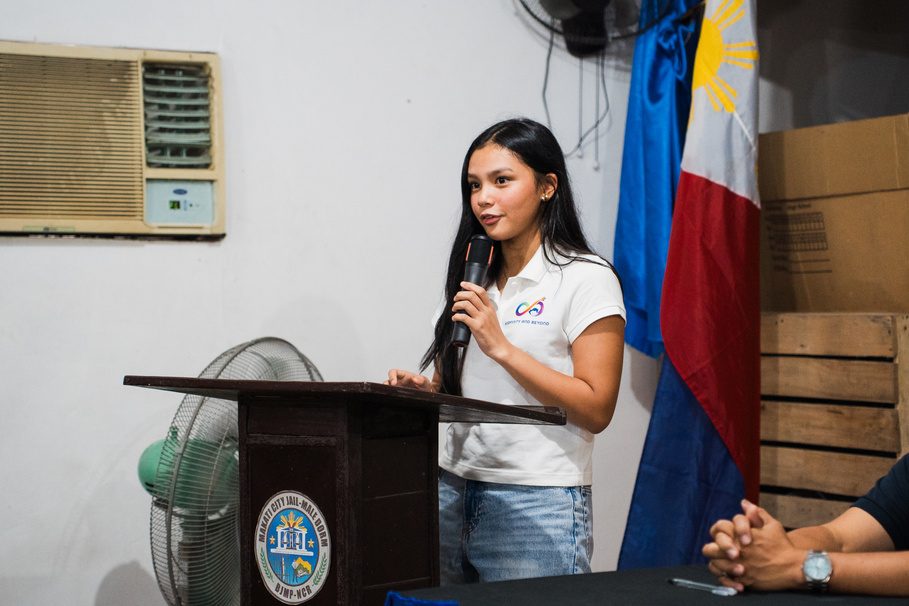 Athalia Suarez speaks into a microphone at a wooden lectern beside the Philippine flag.